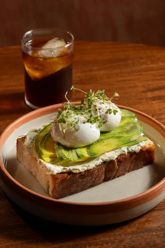 Tostada de aguacate con huevos pochados y microgreens servida con café frío en Nía Bakery cafetería artesanal Cartagena
